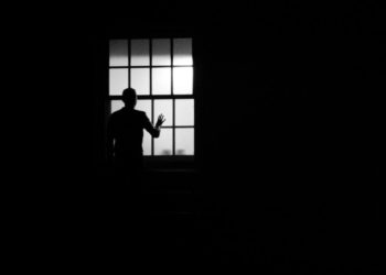Photo en noir et blanc d'un homme regardant par une fênetre
