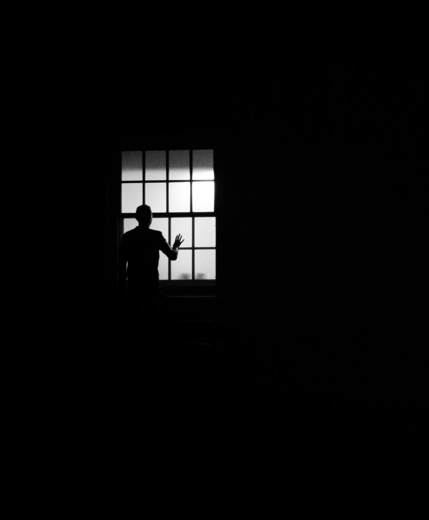 Photo en noir et blanc d'un homme regardant par une fênetre